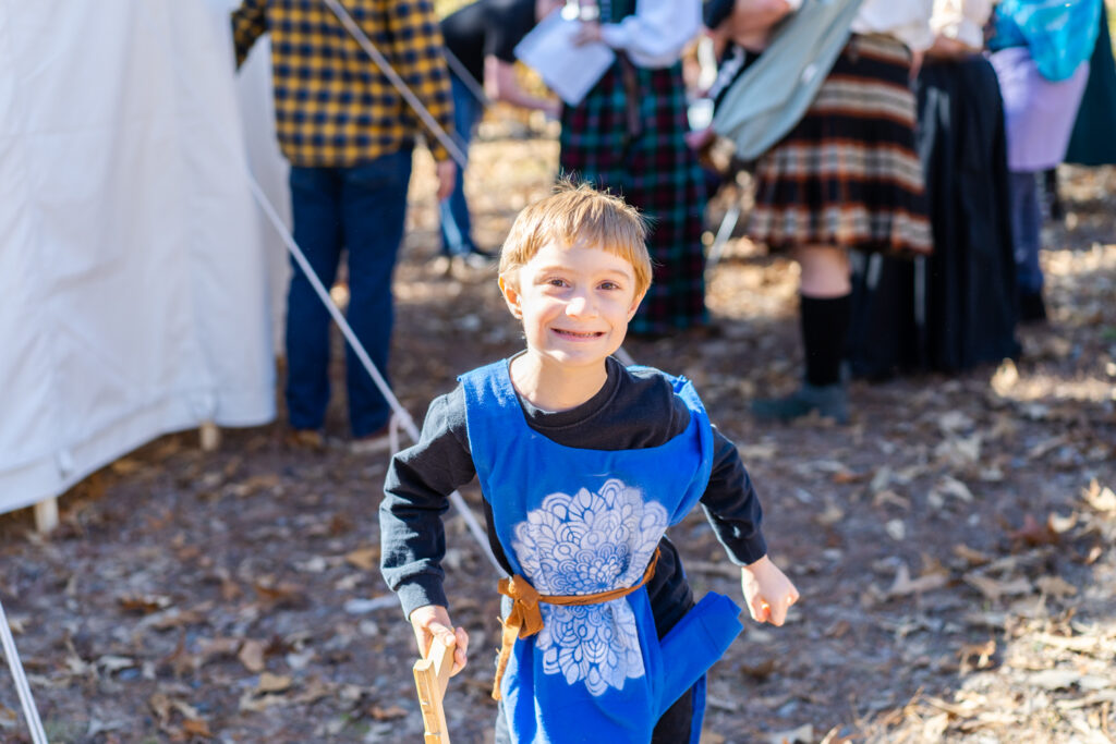 Little boy in a blue jerkin smiles for the camera at the Arkansas Renaissance Festival.