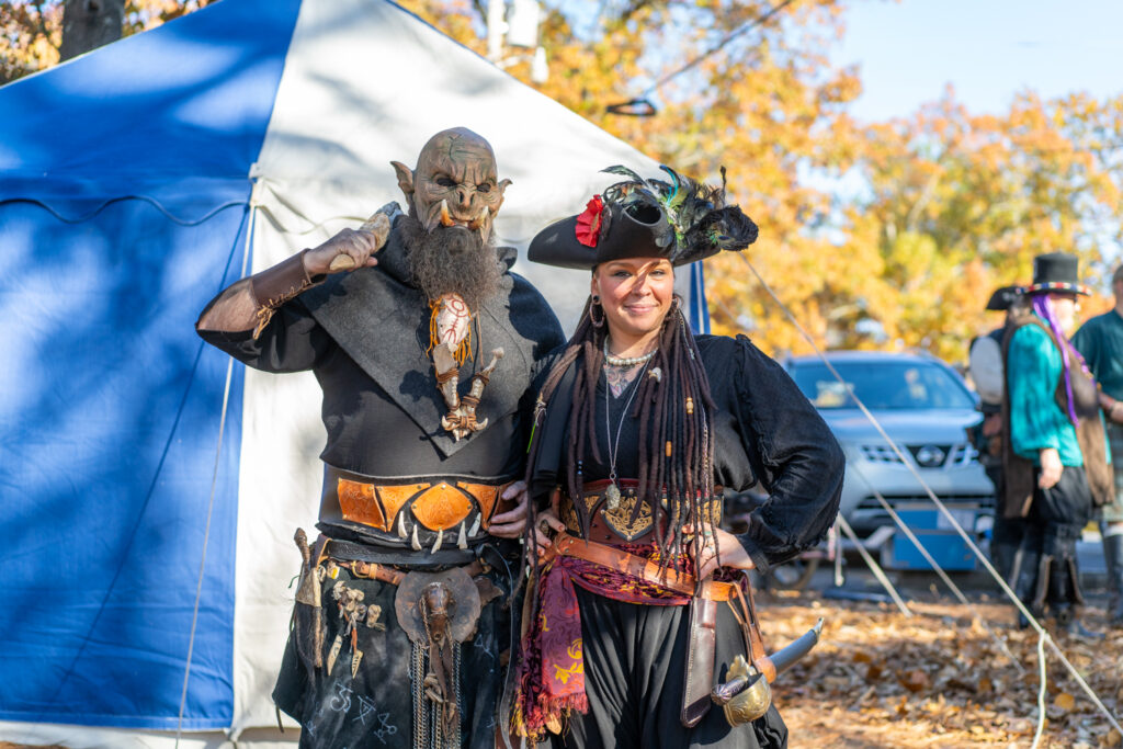 A woman dressed as a pirate and a man dressed as an orc pose in front of a tent at the Arkansas Renaissance Festival.