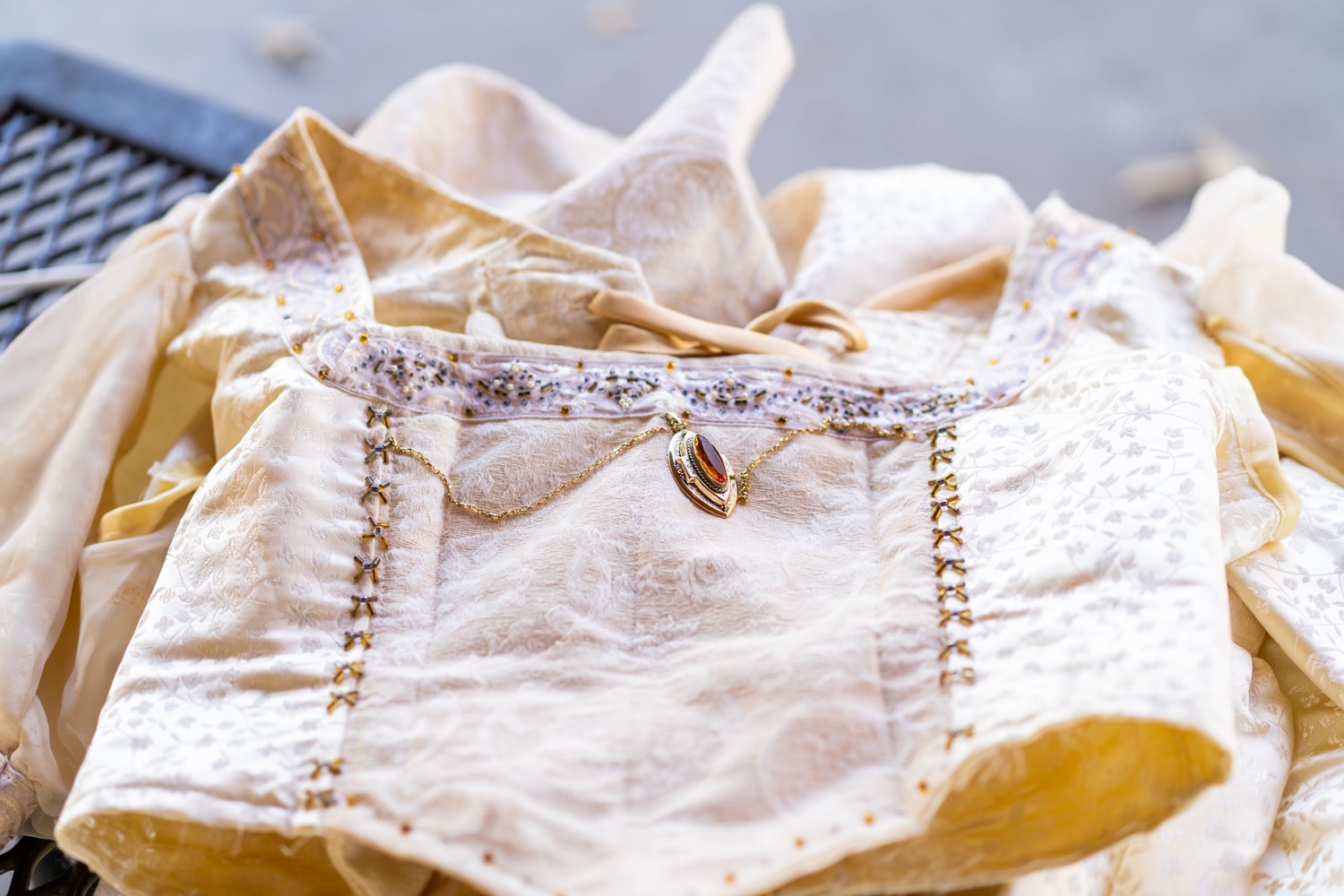 A gold necklace with an orange stone lays on top of a pale yellow medieval corset top.