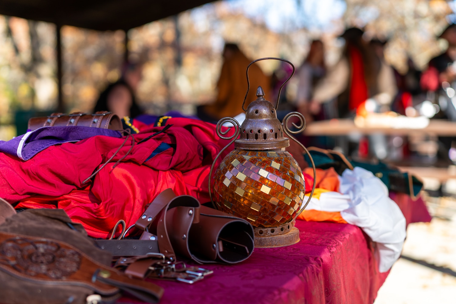 A small red and yellow glass lantern sits on a table with other costumes at the Arkansas Renaissance Festival.