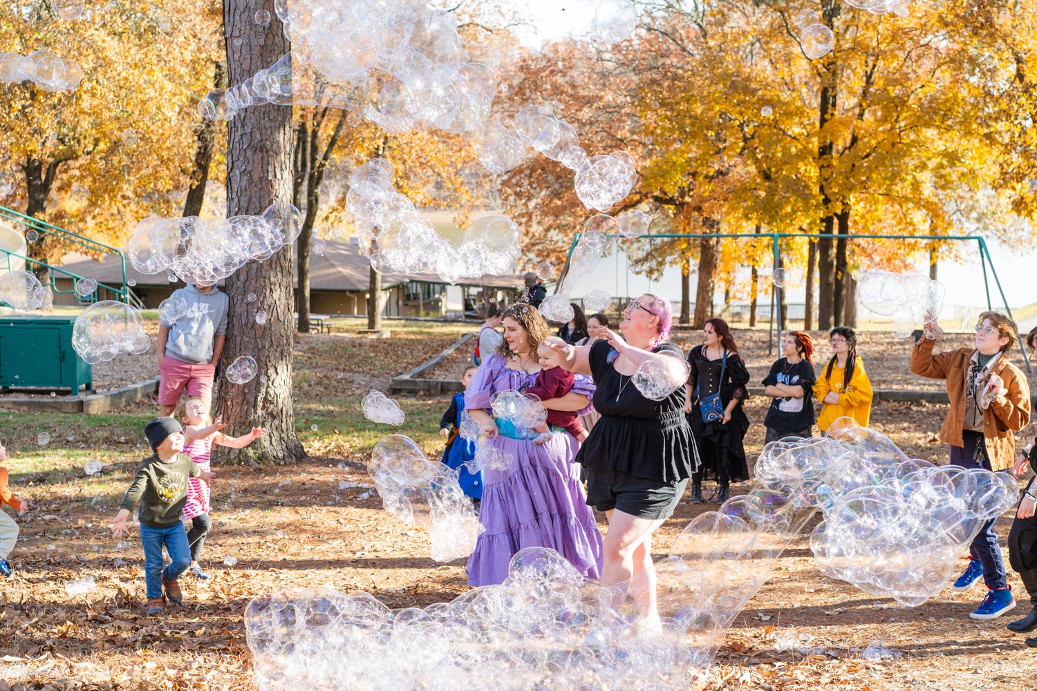 Cosplayers and children chase after large multicolored bubbles in a park in autumn at the Arkansas Renaissance Festival.