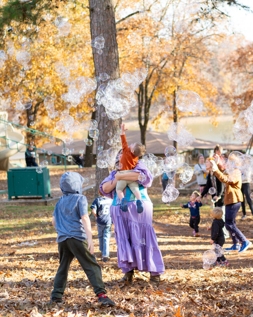 Parents and children chase large multicolored bubbles in a playground at the Arkansas Renaissance Festival.