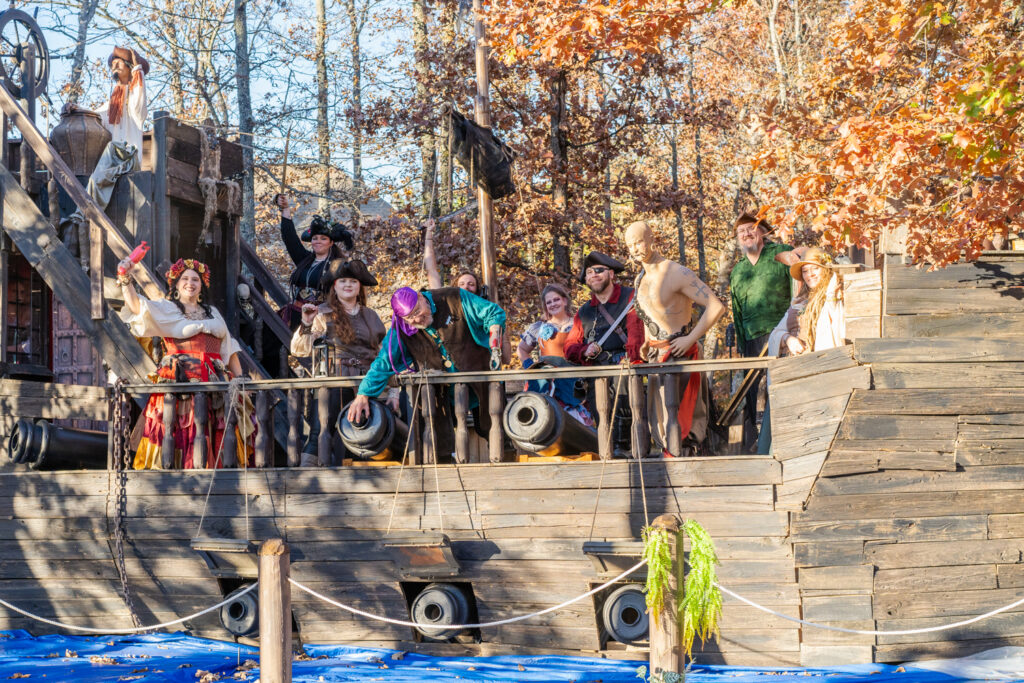 Pirate cosplayers raise fists and swords in the air while standing on a pirate ship at the Arkansas Renaissance Festival.