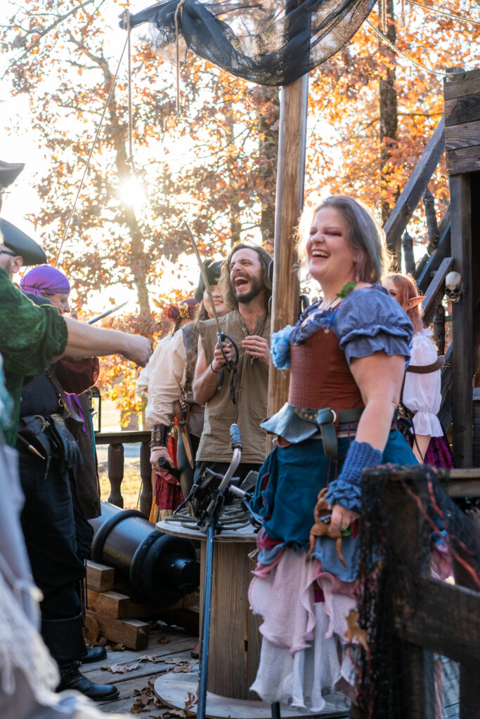 Cosplayers laugh as they stand on a wooden pirate ship at the Arkansas Renaissance Festival.